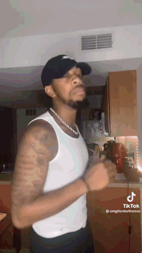 a man wearing a hat and a white tank top is dancing in a kitchen