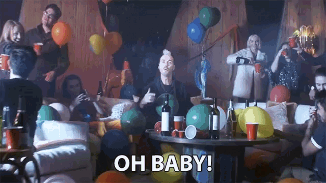a group of people are gathered around a table with balloons and the words oh baby