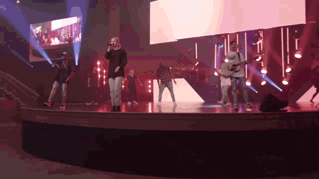 a group of people singing and playing guitars on stage