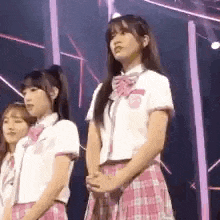 a group of girls in school uniforms are standing on a stage in front of a crowd .