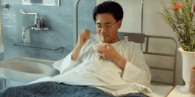 a man is laying in a hospital bed drinking a cup of coffee