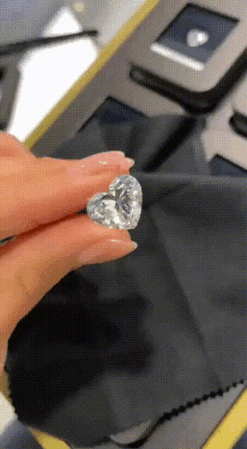 a woman is holding a heart shaped diamond between her fingers
