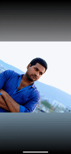 a man in a blue shirt with his arms crossed looks to the side