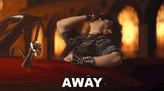 a woman is laying in a red car with the word away written below her