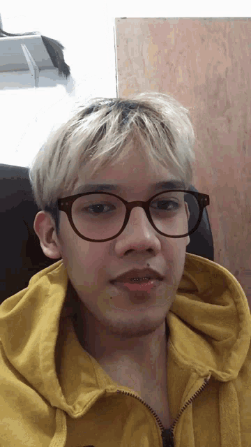 a young man wearing glasses and a yellow sweatshirt