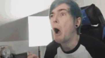 a man with blue hair is sitting in a chair with his mouth open and making a funny face .