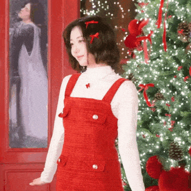 a girl in a red dress is standing in front of a christmas tree .