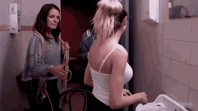 a woman in a white tank top is washing her hands in a bathroom .