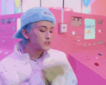 a man wearing a blue hat is holding a cell phone in front of a pink wall