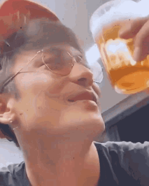 a man wearing sunglasses and a hat is drinking from a glass of beer .
