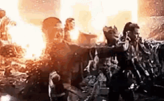 a group of people are standing in front of a fire in a movie scene .
