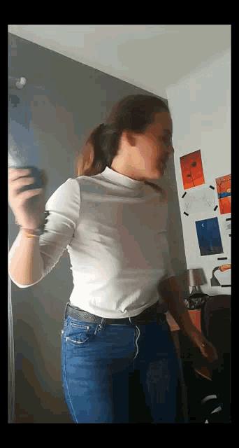 a woman in a white turtleneck and blue jeans is dancing in a room