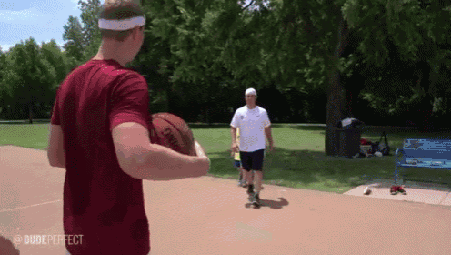 a man in a red shirt is holding a spalding basketball while another man looks on .
