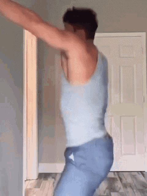 a man in a tank top and jeans is dancing in a room in front of a door .