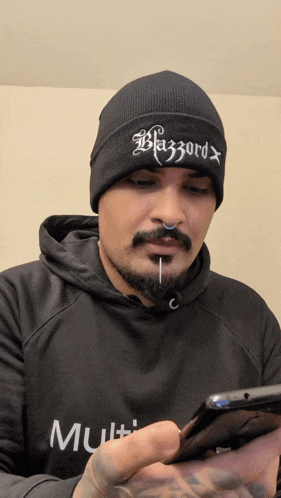 a man wearing a black beanie that says blazzard looks at his phone