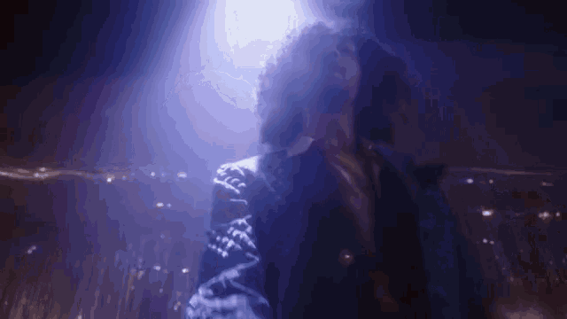 a man with curly hair in a blue suit is dancing in a dark room
