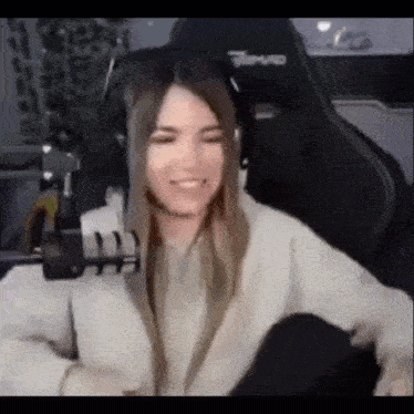 a woman wearing headphones is sitting in a gaming chair and smiling .