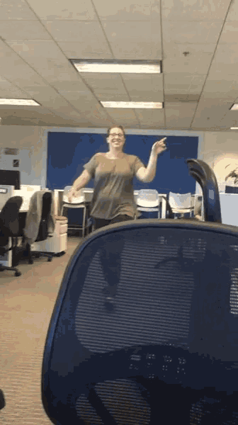 a woman in a grey shirt is standing in an office and pointing