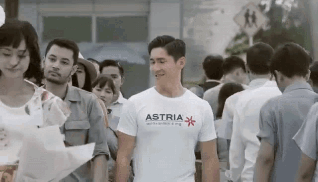 a man wearing a t-shirt that says astra is standing in a crowd of people .