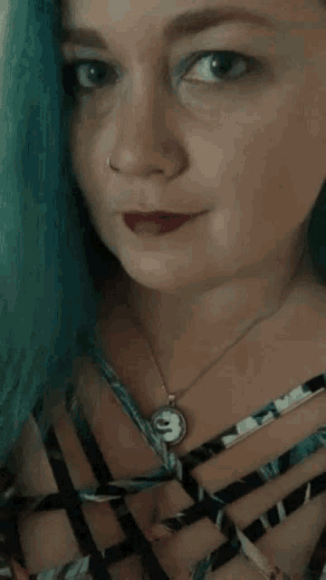 a woman with blue hair is wearing a necklace with a clock pendant
