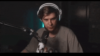 a man wearing headphones and a gray shirt is making a hand gesture in front of a microphone .