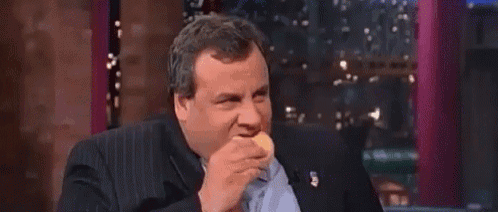 a man in a suit is eating a hamburger while sitting in front of a window .
