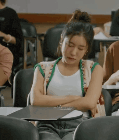a woman is sitting at a desk in a classroom with her eyes closed .