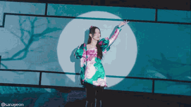 a woman in a green and pink dress is standing in front of a blue wall with the words sanayeon on the bottom