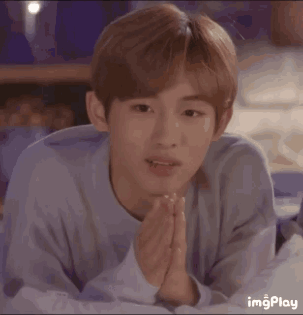 a young boy is laying on a bed with his hands folded in prayer .