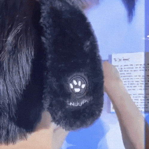 a close up of a person wearing a black dog ear warmer with a paw print on it