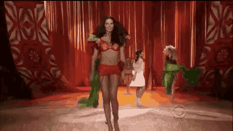a woman is walking down a runway wearing a red bra and shorts .
