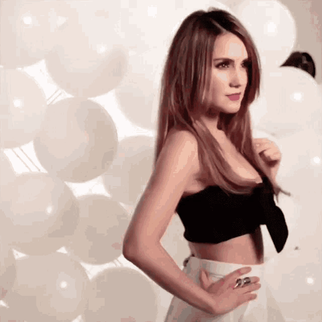 a woman in a black top and white pants is standing in front of a wall of white balloons