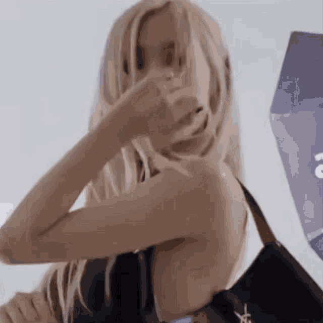 a woman with long blonde hair is holding a black bag and covering her face with her hand .