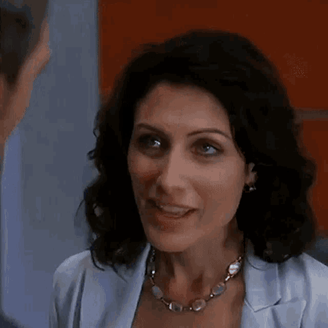 a woman wearing a necklace and earrings is talking to a man in a room .