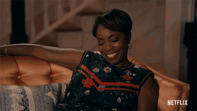 a woman is smiling while sitting on a couch with a netflix logo in the corner