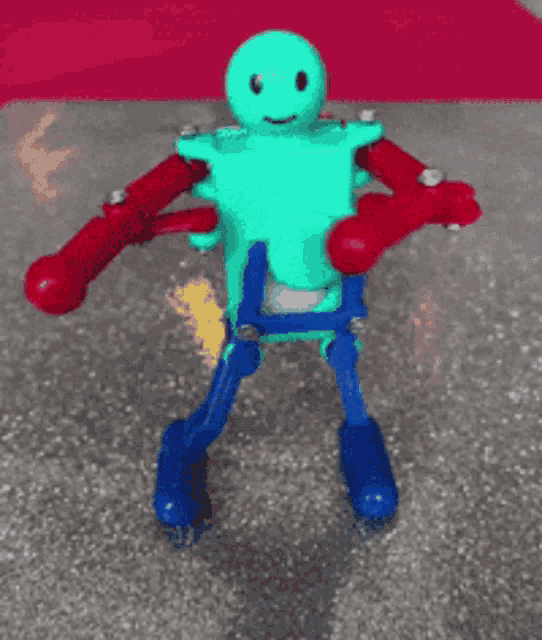 a green toy robot with red arms and legs is standing on a table