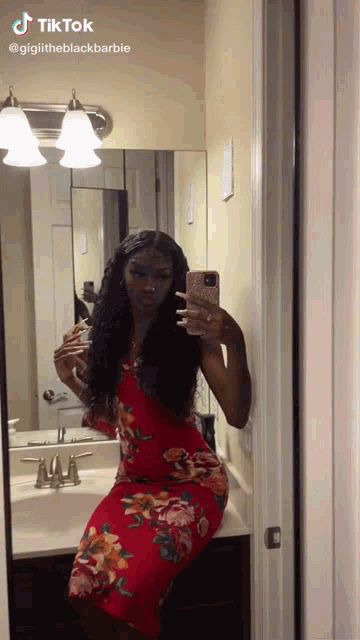 a woman in a red floral dress is taking a selfie in front of a mirror ..