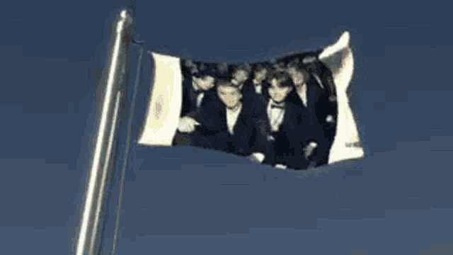 a flag with a picture of a group of men in tuxedos on it is flying in the wind .