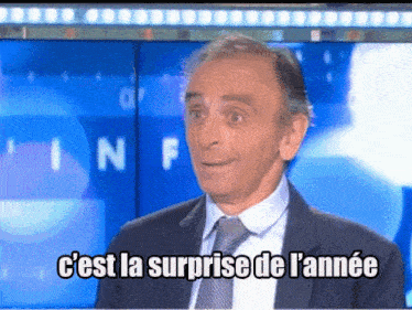 a man in a suit and tie says " c'est la surprise de l' annee " on a screen