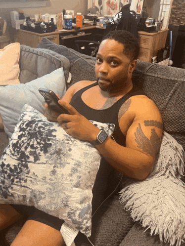 a man is sitting on a couch holding a pillow and a cell phone