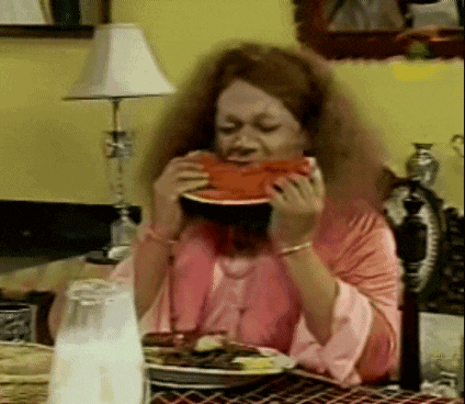 a woman is sitting at a table eating a watermelon