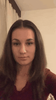 a young woman with long brown hair is taking a selfie in front of a white curtain .