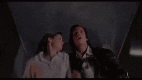 a man and a woman are standing next to each other in a dark room looking up at the sky .