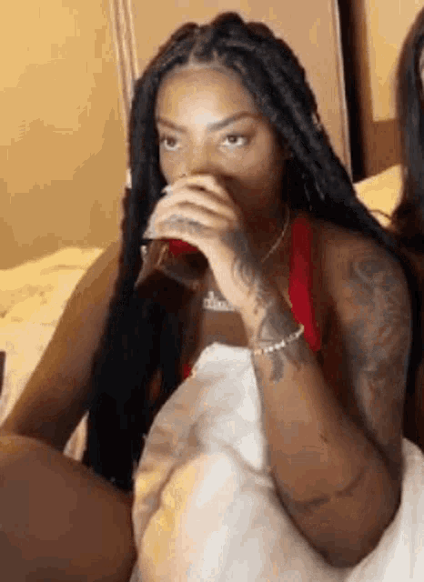 a woman is sitting on a bed drinking a glass of water .