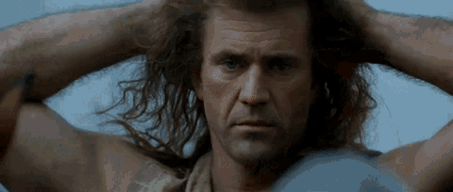 a man with long hair is holding his hands behind his head .