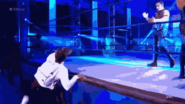 a man in a white hoodie is kneeling down in front of a wrestling ring