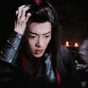 a man with long hair is touching his hair in a dark room