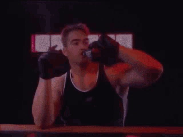 a man wearing boxing gloves and a black tank top is drinking from a bottle .