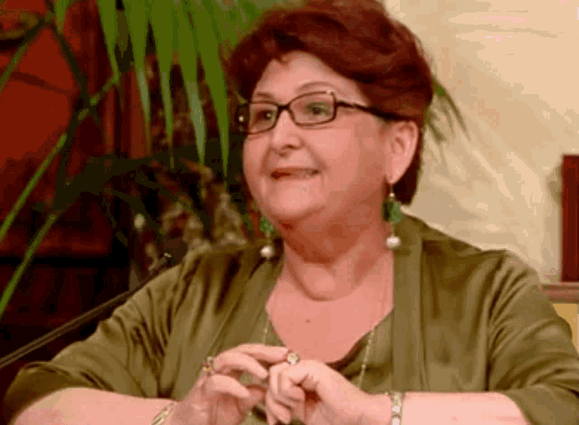 an older woman wearing glasses and a green shirt smiles