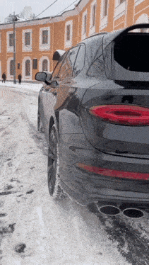 a black car is parked on a snowy street in front of an orange building